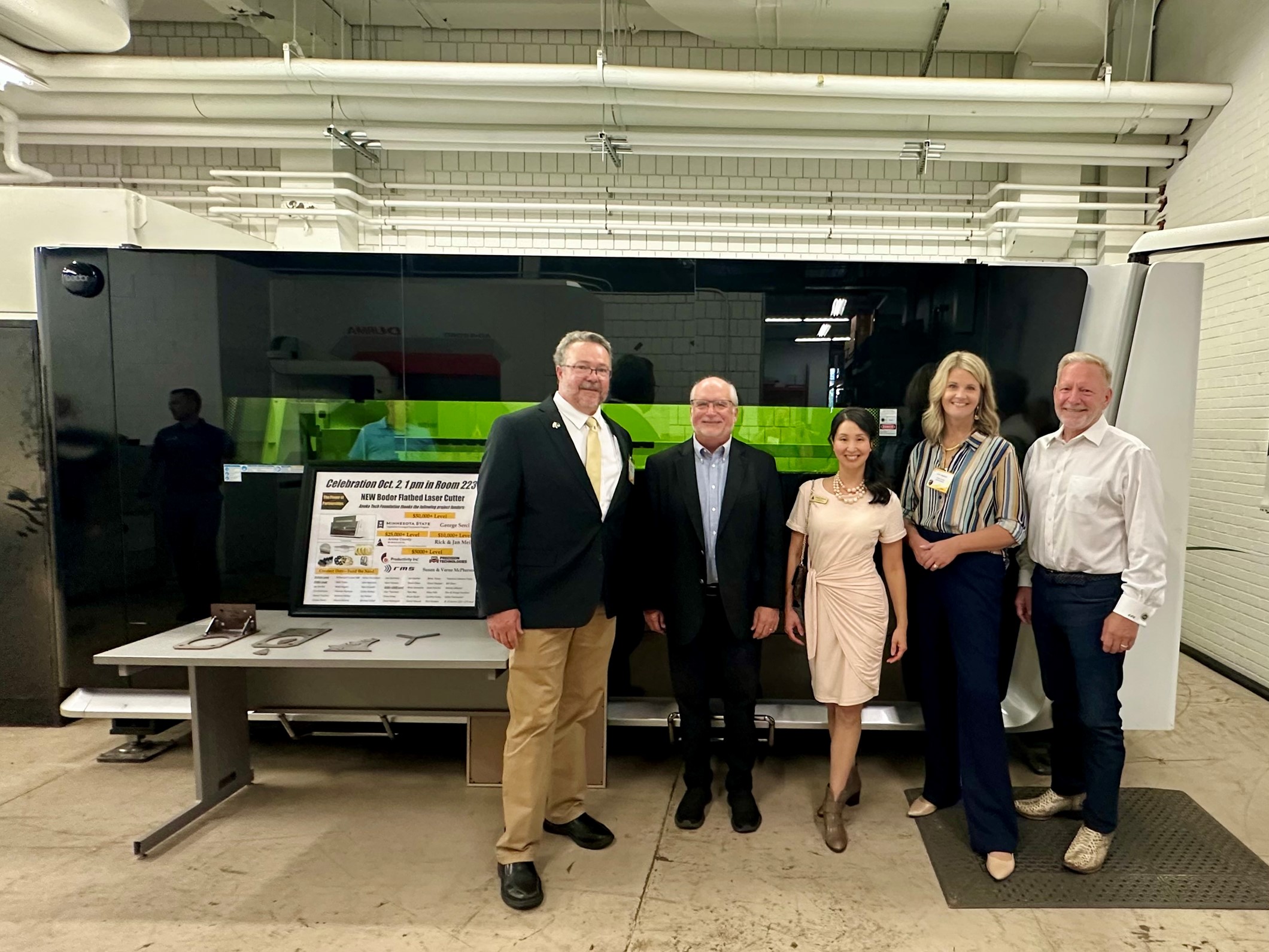 Five individuals posing in front of industrial equipment in a workshop environment.