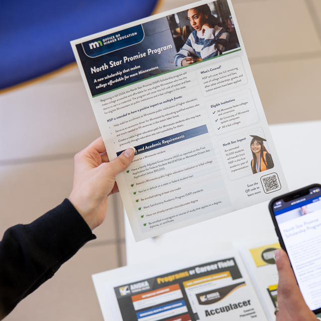 Hands holding a brochure titled "North Star Promise Program" from the Minnesota Office of Higher Education, detailing program benefits and academic requirements. Other educational materials are visible on the table below.